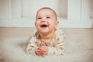 Joyful baby lying on a fluffy rug, smiling and looking upwards indoors.